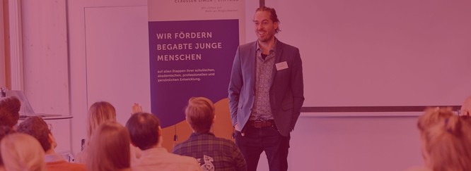 Foto von einem Mann, der einer Gruppe junger Menschen etwas erzählt. Darüber ein rotes Overlay.