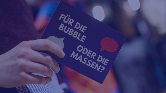 Nahaufnahme einer Hand, die eine Postkarte mit der Aufschrift "Für die Bubble oder die Massen?" hält, Foto mit blauem Overlay