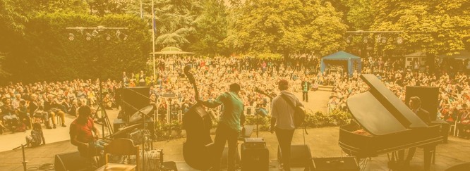 Foto einer Band auf der Bühne, dahinter sieht man das Publikum. Darüber ein gelbes Overlay.